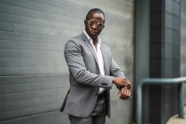 Masculine African American male executive in formal suit and sunglasses revising time on street — Stock Photo