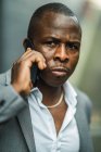 Homme d'affaires afro-américain adulte en costume élégant parlant sur un téléphone portable tout en regardant loin dans la ville — Photo de stock