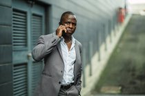 Дорослі афроамериканські бізнесмени у стильному костюмі розмовляють по мобільному, дивлячись у місто. — стокове фото