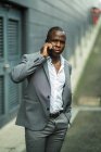 Adult African American businessman in stylish suit talking on cellphone while looking away in city — Stock Photo