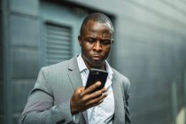 Schwerwiegender schwarzer Chef, der in der Stadt mit dem Handy surft — Stockfoto