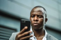 Sérieux noir mâle patron navigation un téléphone portable dans ville — Photo de stock