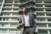 From below of adult well dressed black male executive in sunglasses looking away against multistory house in city — Stock Photo
