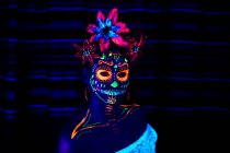 Mulher anônima em máscara de máscaras multicoloridas com flores na cabeça olhando para a câmera na noite de Halloween — Fotografia de Stock