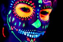 Femme anonyme en masque de mascarade multicolore avec des fleurs sur la tête regardant la caméra la nuit d'Halloween — Photo de stock