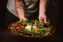 Hands of anonymous person holding a yummy burrata cheese on cold tomato cream with arugula leaves and cherry tomatoes with truffles and peanuts — Stock Photo