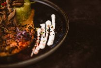 Закрыть вид на урожай вкусное веганское блюдо с цуккини спагетти и колбасные ломтики грибов, покрытые красными ягодами и люцерной капустой на темном фоне — стоковое фото