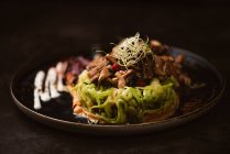 Yummy vegan dish with zucchini spaghetti and sauteed mushroom slices covered with red berries and alfalfa sprouts on dark background — Stock Photo
