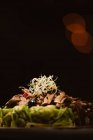 Baixo ângulo de prato vegan gostoso com espaguete de abobrinha e fatias de cogumelos refogados cobertos com bagas vermelhas e brotos de alfafa no fundo escuro — Fotografia de Stock