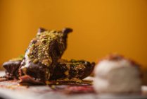 Des brownies savoureux recouverts de beurre d'arachide et de pistaches concassées croquantes près d'une cuillère à glace sur assiette avec sauce au chocolat sur fond jaune — Photo de stock