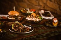 Pratos vegetarianos apetitosos com cogumelos refogados e legumes perto de hambúrguer e sorvete com torrada francesa em mesa de madeira — Fotografia de Stock