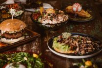 Platos vegetarianos apetitosos con setas salteadas y verduras cerca de hamburguesas y helados con tostadas francesas sobre mesa de madera - foto de stock