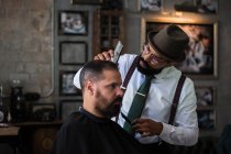 Élégant dandy grave ethnique homme coiffeur coupe cheveux de client adulte avec tondeuse électrique dans le salon de coiffure — Photo de stock