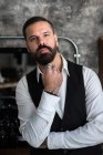 Adult brutal male executive in formal wear and rings touching beard while looking at camera in hairdressing salon — Stock Photo
