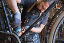 Konzentrierter männlicher Mechaniker mit Bart und Tätowierungen in Handschuhen repariert Fahrrad in moderner Werkstatt — Stockfoto