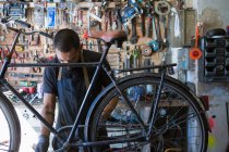 Концентрированный механик-мужчина с бородой и татуировками в перчатках, ремонтирующий велосипед в современной мастерской — стоковое фото