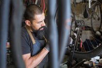 Grave uomo adulto in grembiule e guanti riparazione ruota della bici in garage moderno — Foto stock