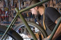 Серйозний дорослий чоловік в фартусі і рукавичках ремонтує колесо мотоцикла в сучасному гаражі — стокове фото