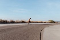 Полное тело молодой бородатый мужчина катается на скейтборде по асфальтовой дороге в сельской местности — стоковое фото