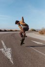 Full body young bearded skater in casual outfit jumping while performing kickflip on skateboard on asphalt road — Foto stock