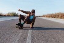 Все тело молодой бородатый мужчина катается на коньках в повседневной одежде выполняя трюк касания земли во время езды по асфальтовой дороге — стоковое фото