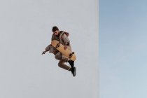 Молодий бородатий активний чоловічий ковзаняр у повсякденному вбранні стрибає під час виконання трюку на скейтборді в скейтпарку — стокове фото