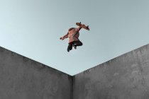 Знизу повний вид на тіло молодого ковзаняра в повсякденному одязі зі скейтбордом, що стрибає на бетонній рампі в скейт-парку виконує трюк — стокове фото