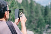 Вид ззаду анонімний чоловічий похід у сонцезахисних окулярах фотографії улюблених жінок на мобільний телефон під час поїздки — стокове фото