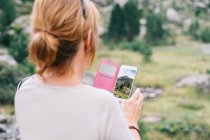 Back view femelle anonyme prenant des photos sur smartphone d'étonnantes montagnes verdoyantes pierreuses dans la vallée de la ruda dans les pyrénées catalanes — Photo de stock