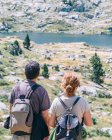 Blick von anonymen Backpackern auf den See zwischen Bergen mit Steinen und Bäumen während der Sommertour — Stockfoto