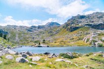 Magnífico paisaje de áspera cordillera rocosa que rodea el tranquilo lago azul bajo el cielo azul claro en el soleado día de verano en los Pirineos Catalanes - foto de stock