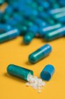 Високий кут вмісту ліків, що виливаються з синьо-кольорової капсули на жовтому тлі — стокове фото