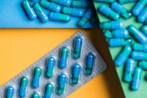 Сверху пластиковые блистерные упаковки с голубыми медицинскими капсулами размещены на желтом, зеленом и синем фоне — стоковое фото