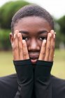 Giovane tenera donna afroamericana con i capelli corti che coprono il viso mentre guarda la fotocamera in città il giorno d'estate — Foto stock