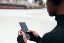 Обрезание анонимных сообщений этнической женщины на мобильном телефоне с черным экраном в городе — стоковое фото