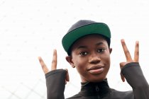 Angle bas de jeune femme afro-américaine en tenue décontractée regardant la caméra avec le doigt vers le haut en plein jour — Photo de stock
