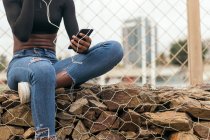 Crop femme noire écouter de la musique avec un téléphone portable et écouteurs — Photo de stock