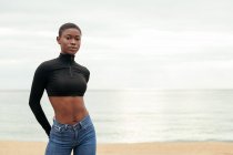 Junge sanfte Afroamerikanerin in lässiger Kleidung blickt an der Küste des Ozeans in die Kamera — Stockfoto
