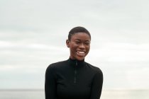 Giovane donna afroamericana gentile in abiti casual guardando la fotocamera sulla costa dell'oceano — Foto stock