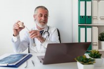 Старший чоловічий ортодонт, який демонструє щелепу, виступає проти нетбука під час відеочату за столом у лікарні — стокове фото