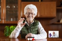 Freundliche ältere Frau zeigt bei Videochat im Haus Grußgeste gegen Tablet — Stockfoto