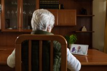 Vista posterior de la paciente anciana anónima en auriculares TWS hablando con el médico en la tableta durante la videollamada en casa - foto de stock