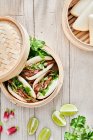 From above of tasty steamed baozi buns with radish and cucumber slices with meat and fresh cilantro on table — Stock Photo