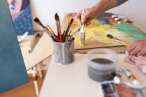 Crop unrecognizable male painter using professional brush during painting process on carton sheet near art tools in workroom — Foto stock
