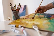 Обрізати невпізнаваного художника-чоловіка, використовуючи професійну пензлик під час малювання на картоні біля художніх інструментів у робочій кімнаті — стокове фото