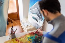 Crop unrecognizable male painter using professional brush during painting process on carton sheet near art tools in workroom — Foto stock