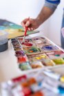 Crop anonymous male painter mélange des peintures avec pinceau en utilisant une palette d'aquarelles tout en travaillant dans un studio d'art — Photo de stock