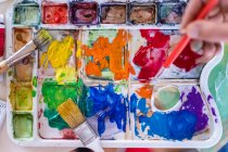 Crop anonymous painter mixing paints with brush using watercolor palette while working in art studio — Stock Photo