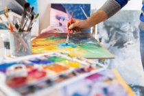 Ernte unkenntlich männlichen Maler mit professionellen Pinsel während des Malprozesses auf Karton Blatt in der Nähe von Kunstwerkzeugen in der Werkstatt — Stockfoto