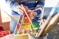 Ernte anonymen männlichen Maler Mischen von Farben mit Pinsel mit Aquarellpalette während der Arbeit im Kunstatelier — Stockfoto